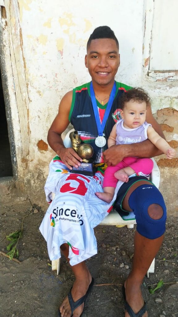GALINDO con su hija de 5 meses y la camiseta que rifa para costear gastos de la operación de rodilla. / FOTO: EL PILÓN.